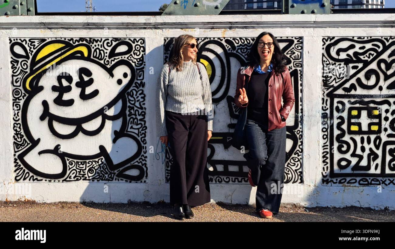 Due amici felici che sorridono e si appoggiano a un muro di graffiti sul ponte ferroviario di Primrose Hill nel nord di Londra. Foto Stock