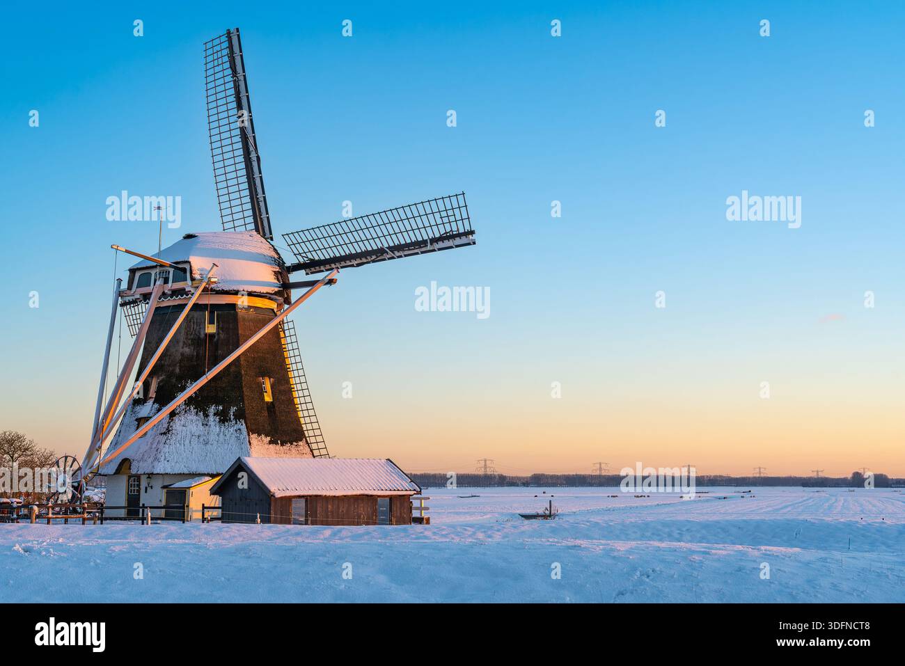 Storico mulino a vento olandese nel paesaggio invernale innevato sotto il cielo blu Foto Stock