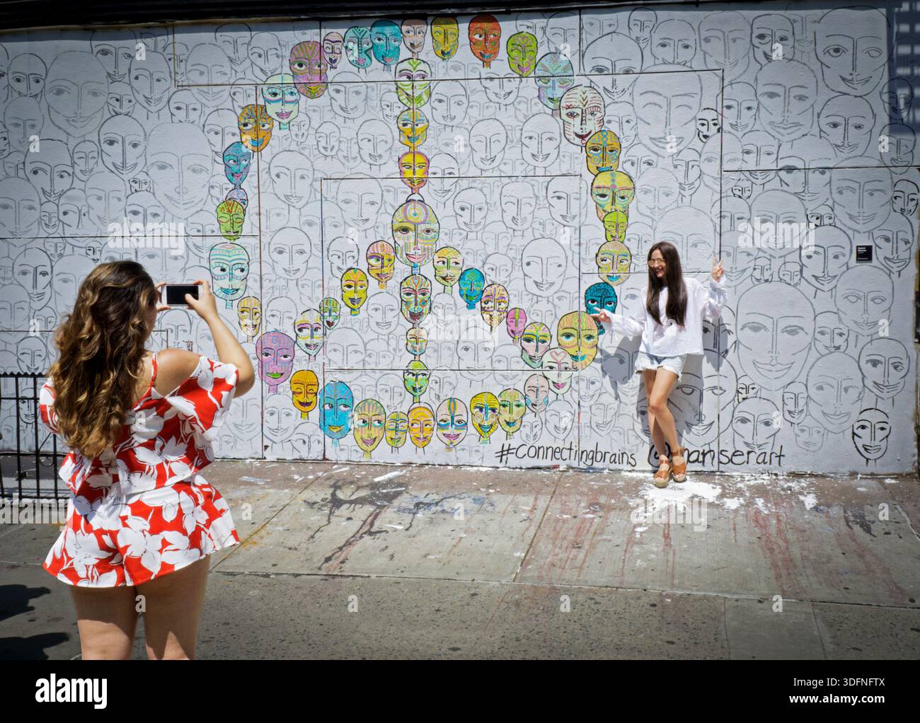 I turisti posano per una foto a un muro con un gigantesco simbolo di pace. Nella sezione NOLITA del centro di New York Foto Stock