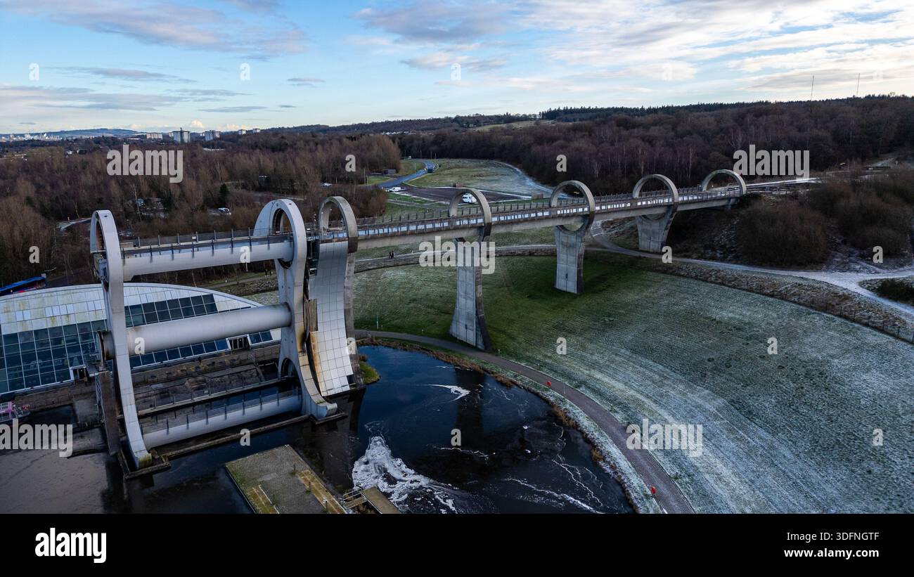 Una vista aerea della ruota di Falkirk, un ascensore per barche rotante, con un canale, il paesaggio circostante e edifici lontani sotto un cielo nuvoloso. Foto Stock