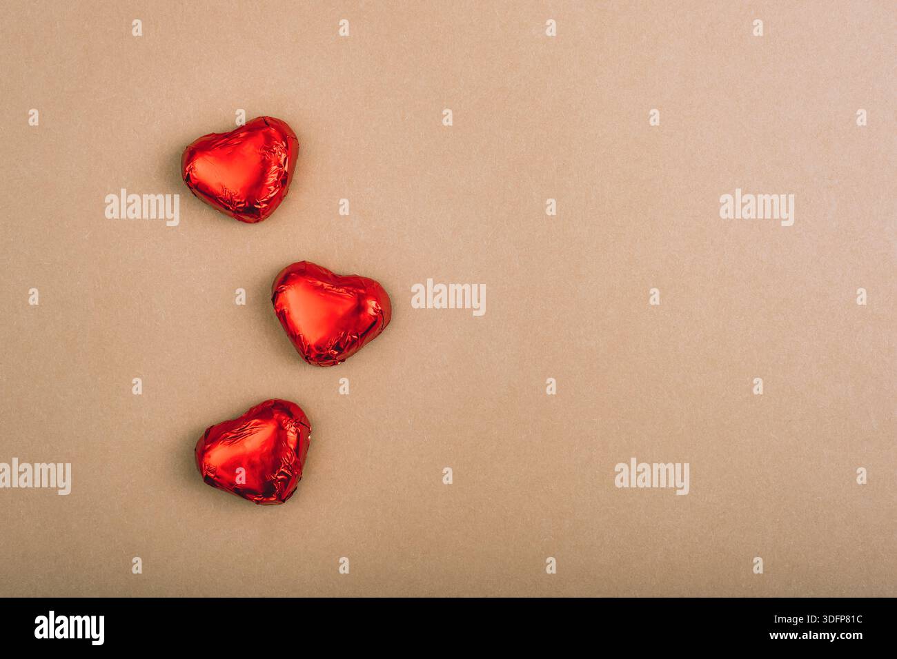 Tre cuori di cioccolato avvolti in un foglio rosso su sfondo di carta marrone con spazio per le copie. Foto Stock