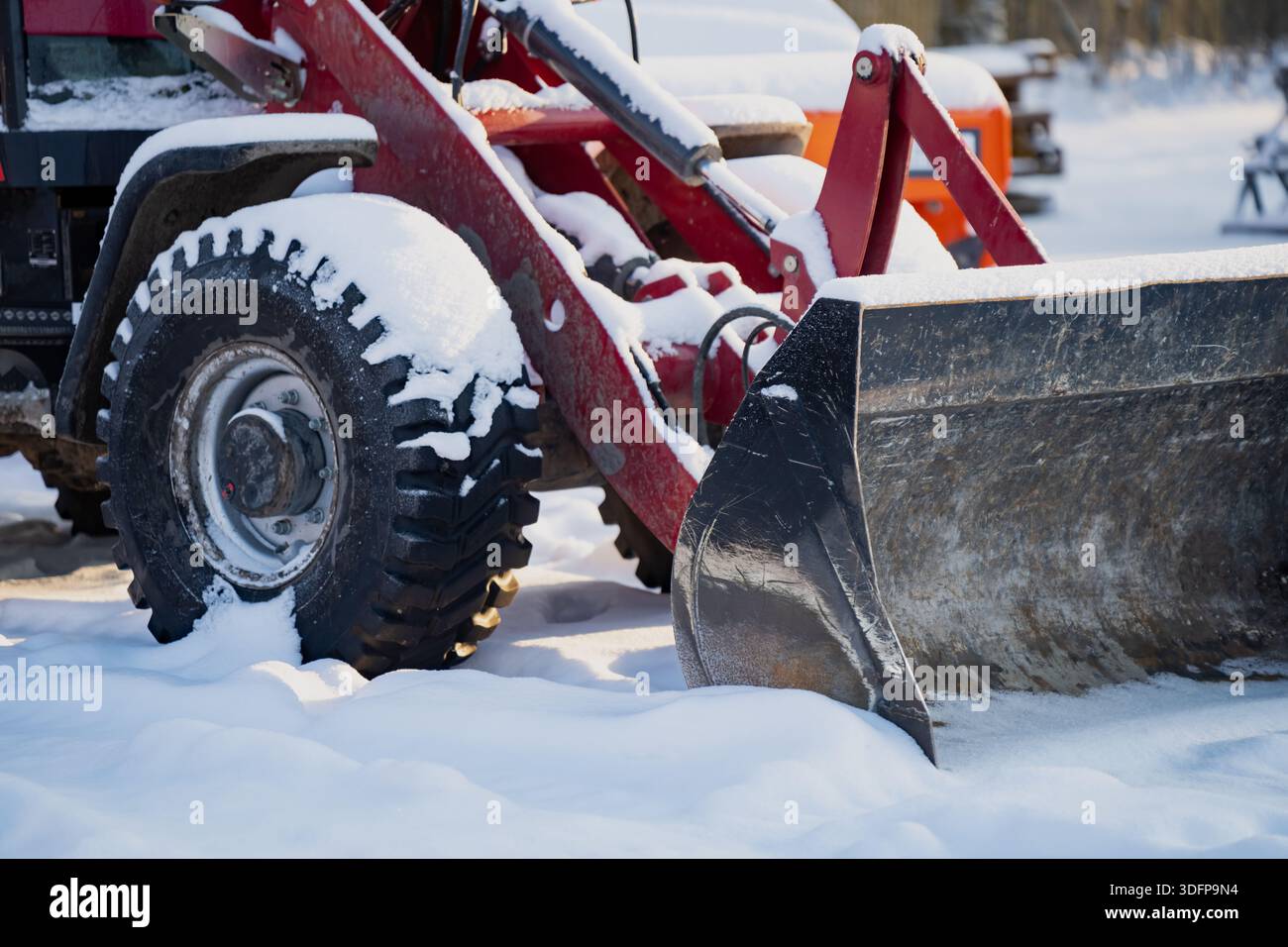 Attrezzatura caricatore frontale del trattore agricolo con pneumatico innevato e benna in acciaio sporco, vista ravvicinata dell'attrezzatura invernale utilizzata per lo smontaggio della neve e per lavori in campagna Foto Stock