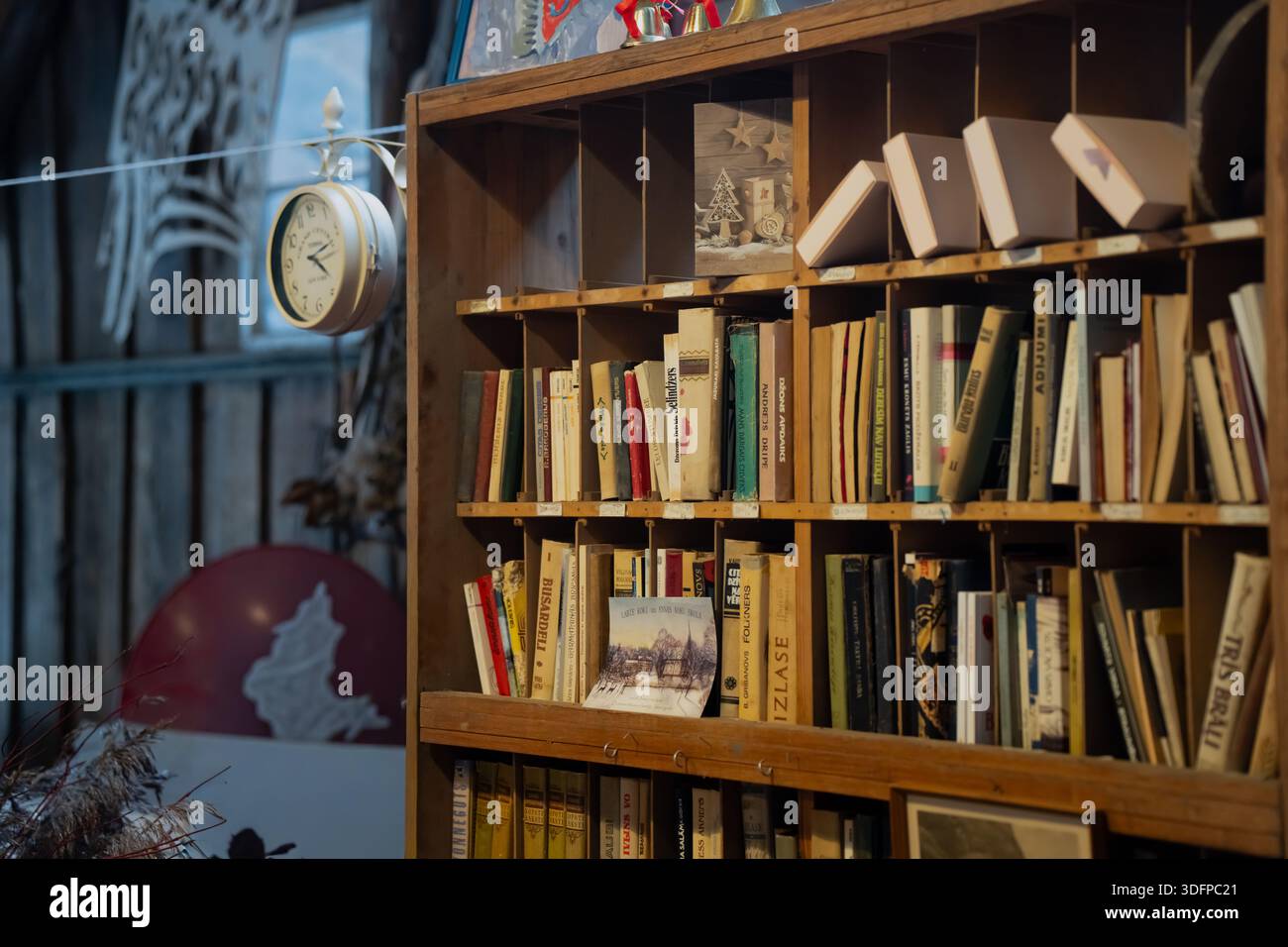 libreria acustica in legno piena di vecchi libri e piccole cartoline, angolo biblioteca interno caldo con orologio da parete appeso e sfondo officina in soffice ligh Foto Stock