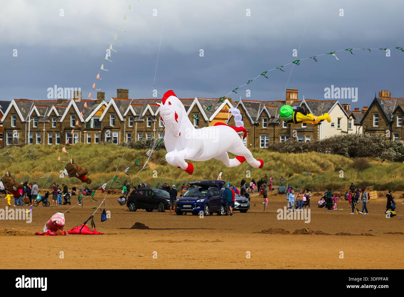 Gigantesco aquilone gonfiabile che vola sopra la spiaggia durante una festa degli aquiloni a Lytham St Annes, con spettatori e veicoli sulla sabbia. Foto Stock