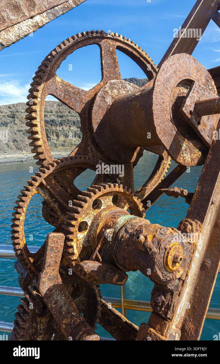 Ingranaggi arrugginiti da un vecchio paranco che mostrano degrado industriale lungo la costa Foto Stock