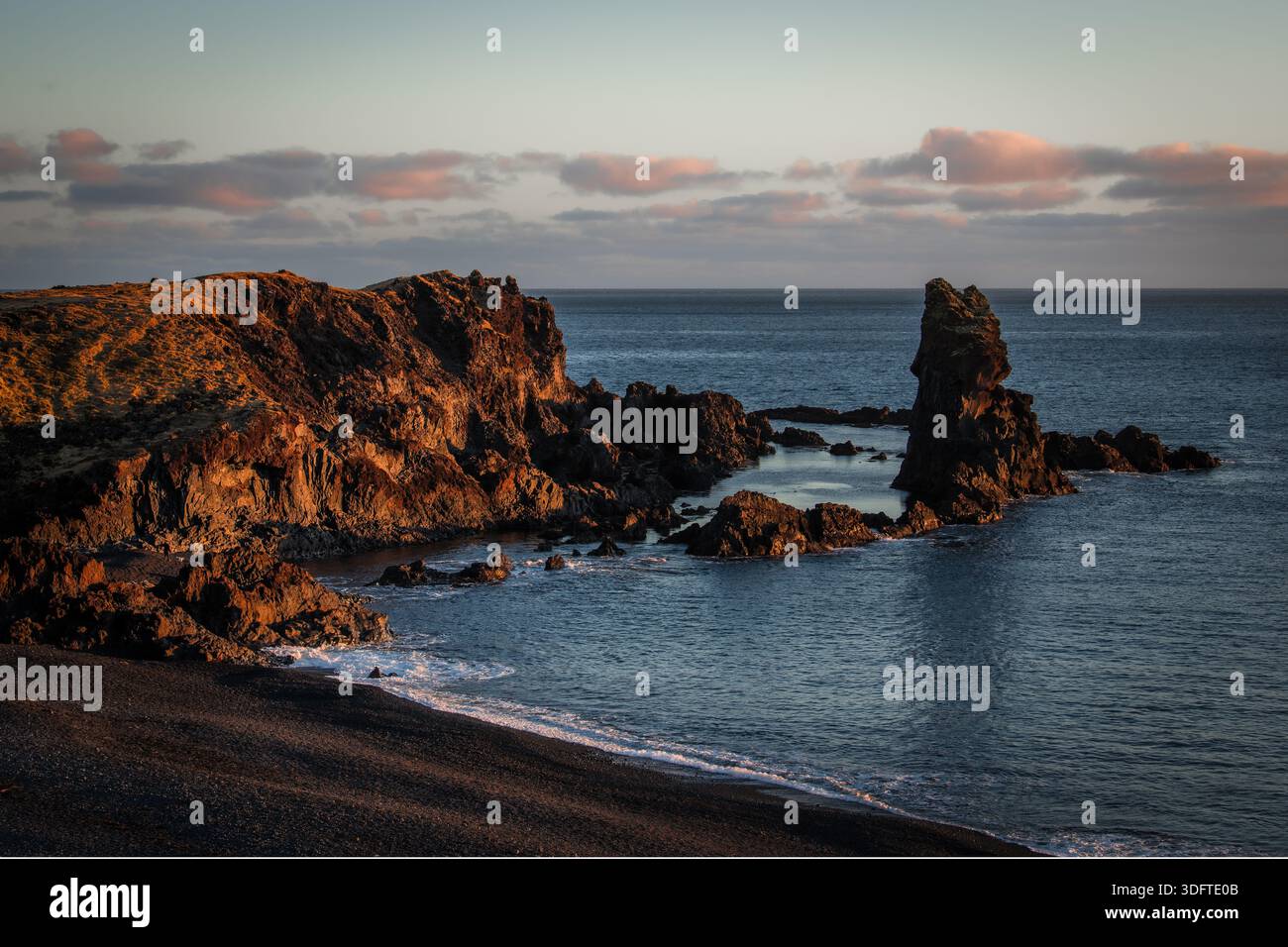 Vista della costa frastagliata dove le scure rocce vulcaniche incontrano il mare blu sereno sotto un cielo pallido, la penisola di Snaefellsnes, Grundarfjordur, West IC Foto Stock