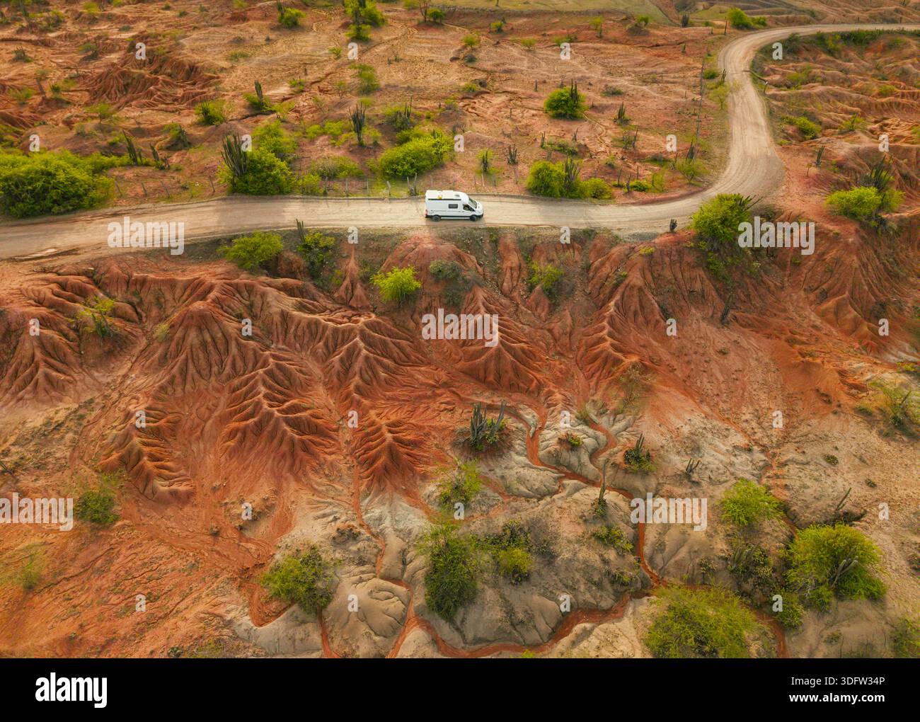 Vista aerea di un camper solitario che attraversa una strada polverosa nel vibrante paesaggio di terracotta del deserto Tatacoa, Huila, Colombia. Foto Stock