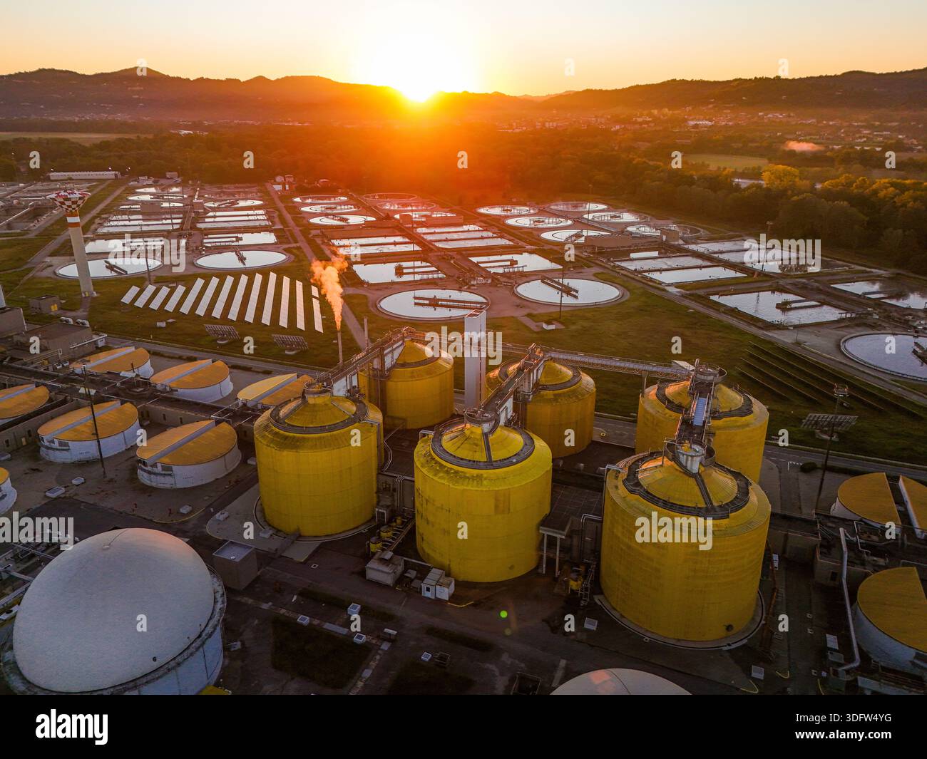 Vista aerea delle vasche dorate dell'impianto di trattamento delle acque reflue che brillano sotto il caldo tramonto, un netto contrasto con il paesaggio industriale, le acque reflue Foto Stock