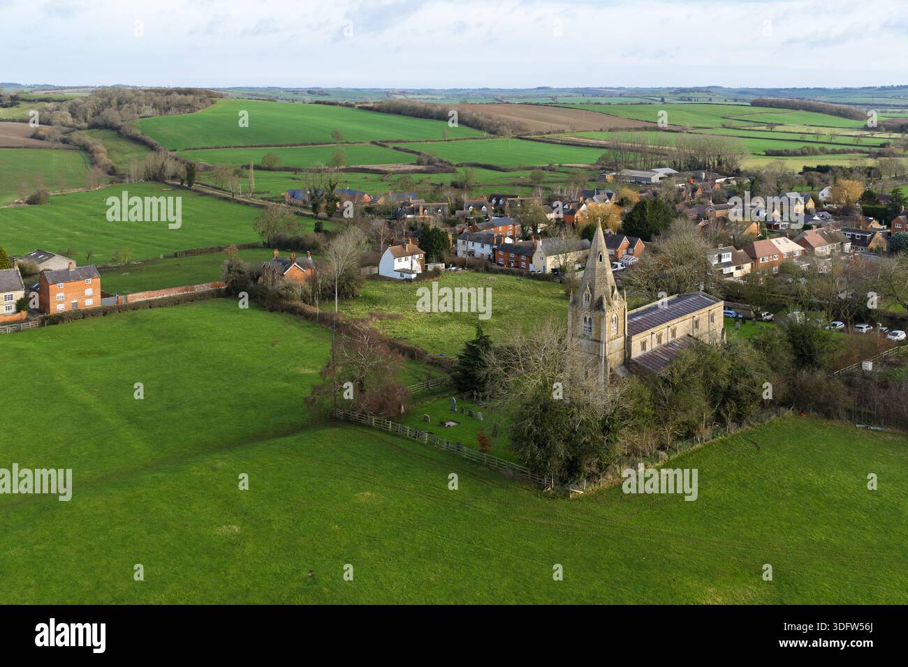 Veduta aerea di una guglia della chiesa in pietra che perfora lo skyline tra verdi campi ondulati e il fascino pittoresco del villaggio, Market Harborough, Inghilterra, United King Foto Stock