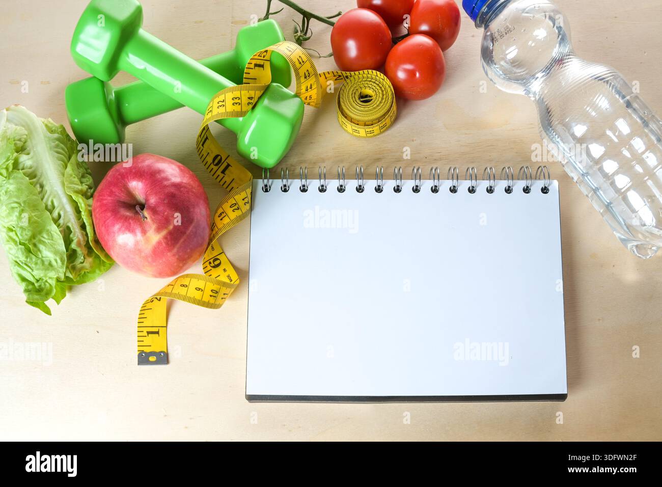 Notebook con anello vuoto e nozioni di base per il fitness come mela, verdure, bottiglia d'acqua e manubri, mockup per un elenco di obiettivi, vita dimagrante e sana Foto Stock