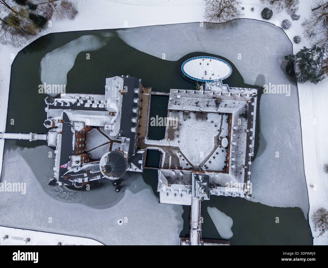 Castello coperto di neve con cortile centrale e fossato ghiacciato forma una scena invernale simmetrica, circondato da terreni ghiacciati e da un paesaggio sereno. Foto Stock