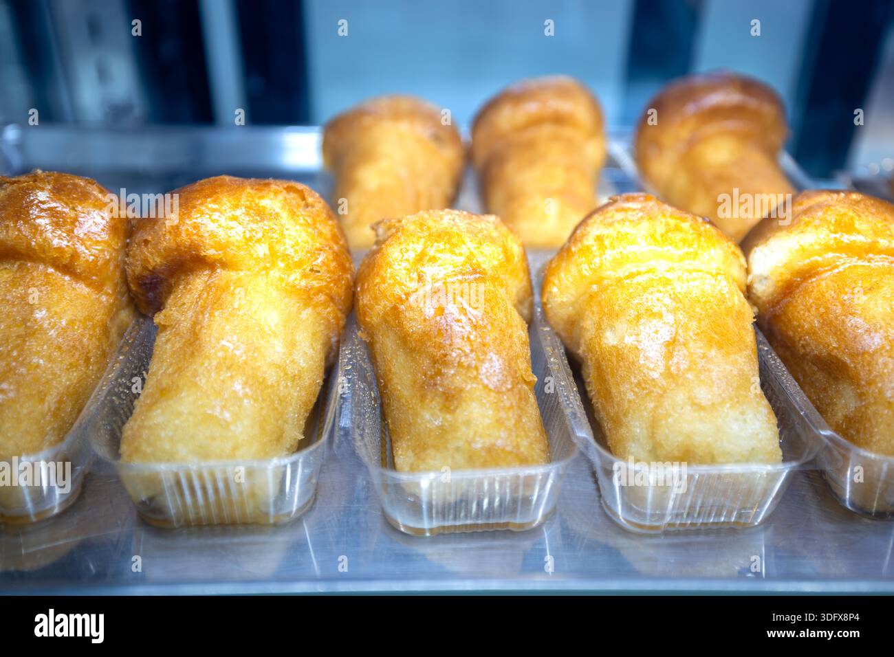 File di dolci al rum babà morbidi e sciropposi presentati in singoli contenitori trasparenti. Un classico dessert napoletano, dorato e umido, pronto per la vendita in un Foto Stock