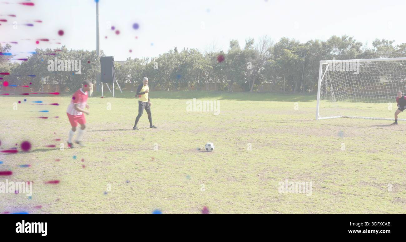 Giocatore in campo esterno in divisa rossa che si sposta verso il pallone da calcio su un campo erboso, pettorale giallo, altoparlante Foto Stock