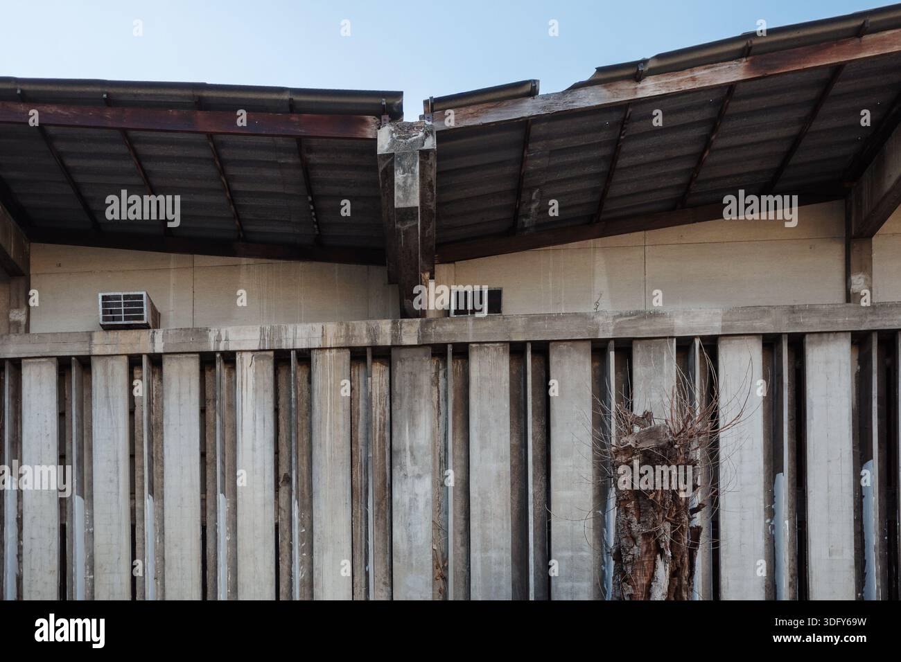 Una foto dettagliata di un antico edificio industriale caratterizzato da un motivo ritmico di pinne verticali in cemento, un tetto ondulato con travi in legno e una foglia Foto Stock