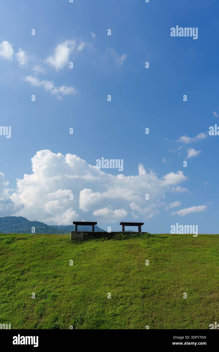 Due panchine di legno sulla cima di una collina erbosa sotto le nuvole e il cielo blu Foto Stock