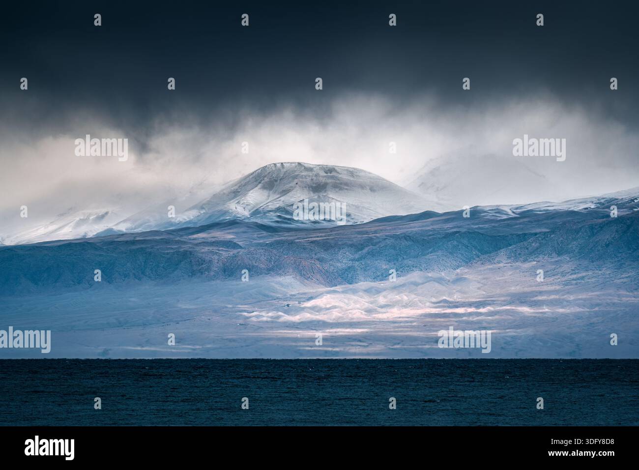 Suggestivo paesaggio lunare di montagne innevate, natura selvaggia e cielo coperto sopra l'oceano scuro in un clima tempestoso Foto Stock