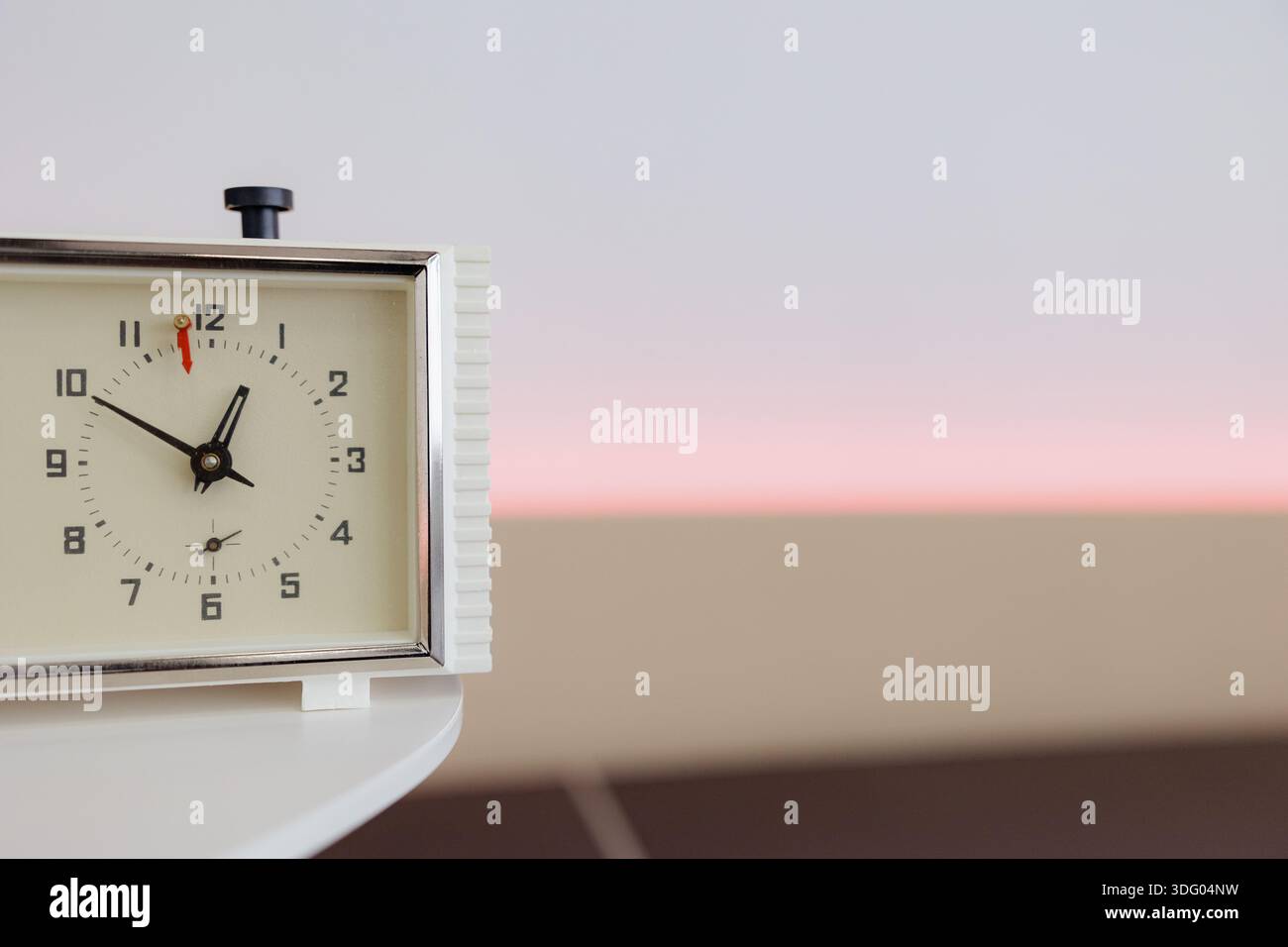 Un orologio vintage si siede graziosamente su un tavolo, con uno sfondo pastello chiaro che illumina la stanza. Il tempo riflette i momenti tranquilli. Foto Stock
