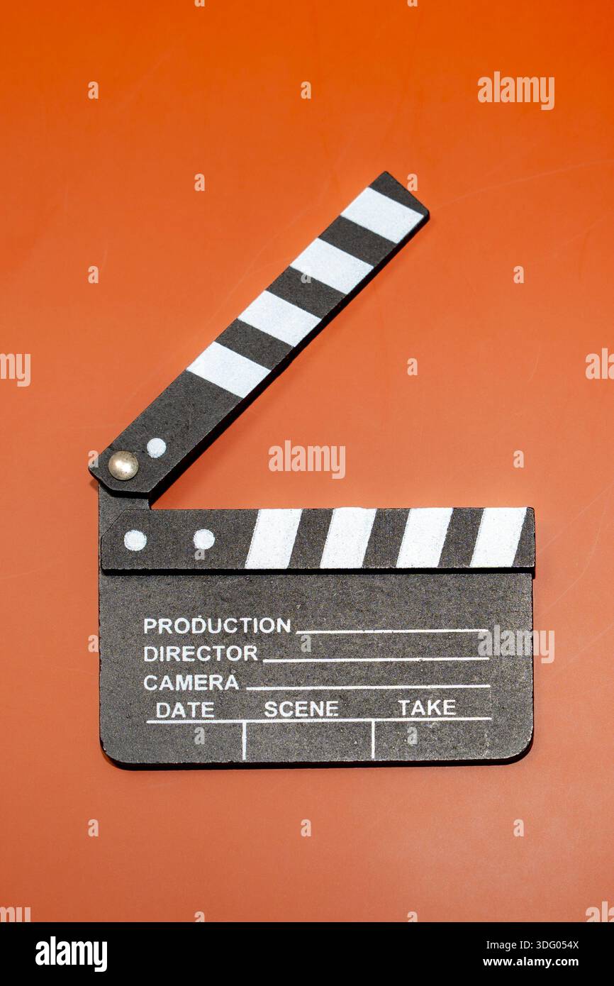 Una lavagna a fogli mobili su sfondo arancione, utilizzata nell'industria cinematografica. L'ardesia viene aperta per indicare l'inizio di una pellicola. Foto Stock