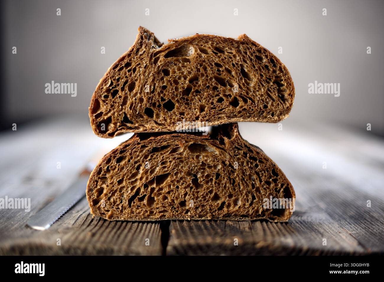 Due metà di pane fresco a base di lievito madre di segale a sezione su un rustico pannello di legno. Pagnotta artigianale in stile fattoria catturata dalla calda luce naturale Foto Stock