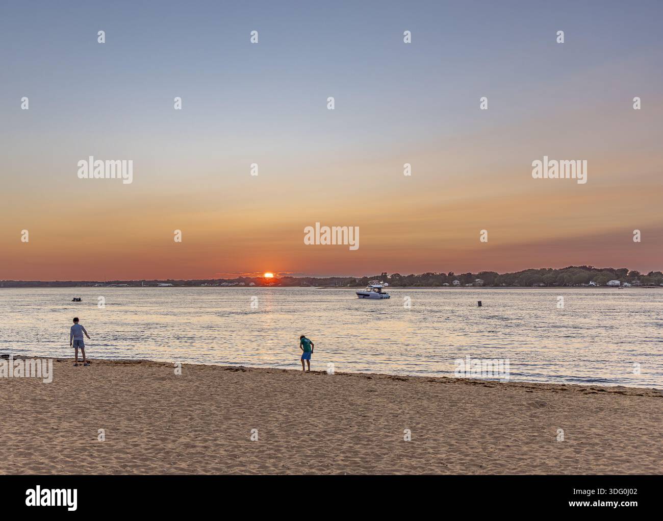 due bambini si godono la spiaggia a mezzaluna mentre il sole tramonta sullo sfondo Foto Stock
