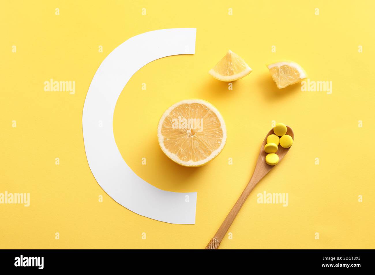 Cucchiaio con pillole di vitamina C, fette di limone e lettera di carta su sfondo giallo Foto Stock