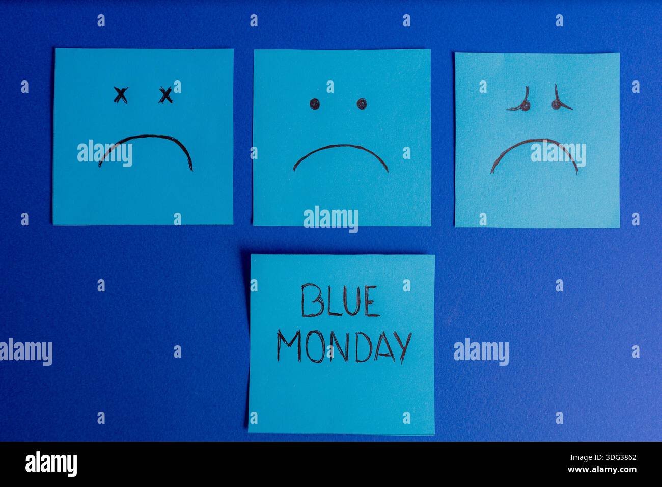 Composizione simmetrica con tre note adesive che mostrano volti tristi sopra una nota centrale con testo Blue Monday su sfondo blu. Foto Stock