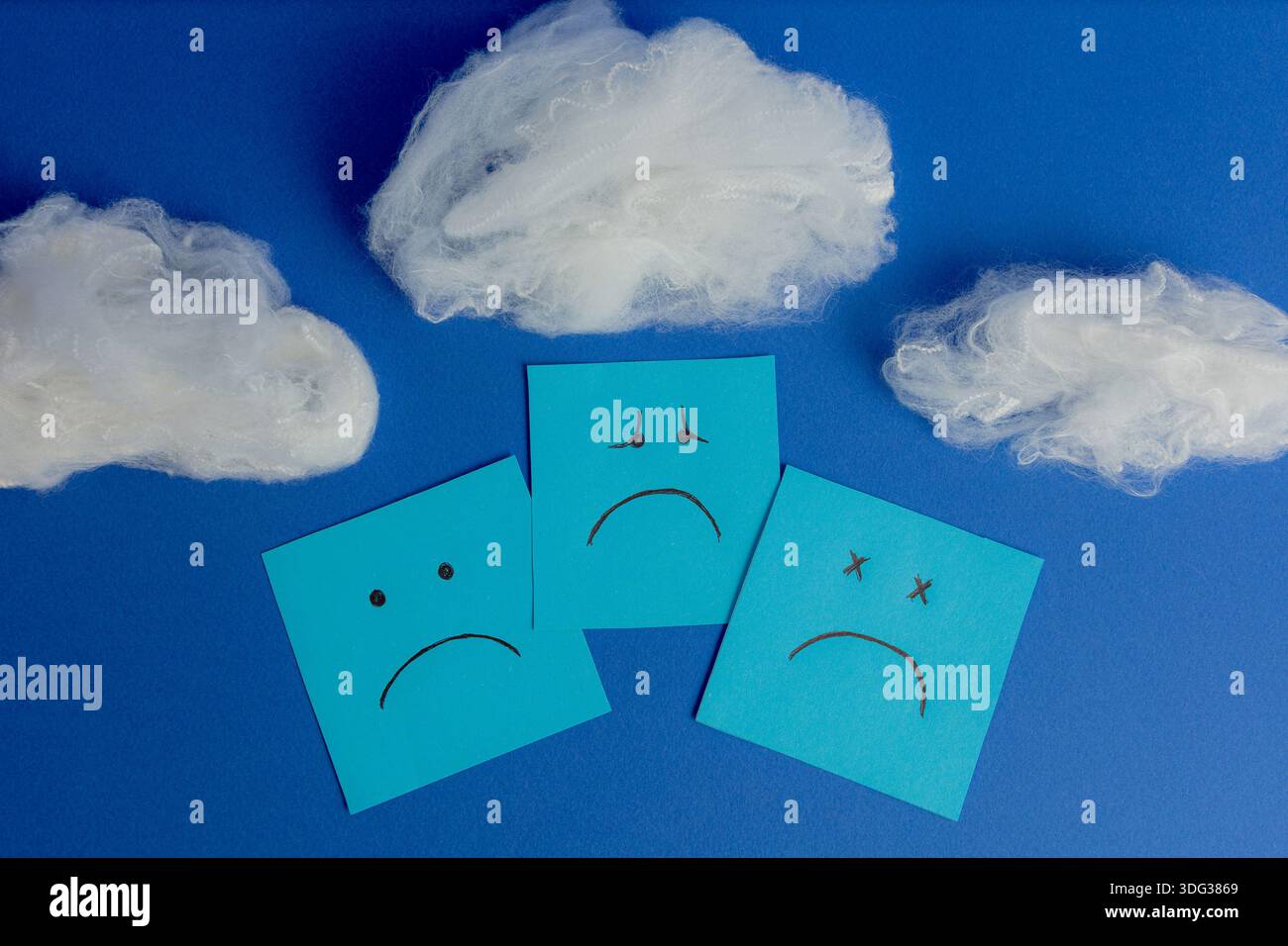 Tre note appiccicose con diverse espressioni di tristezza e depressione sovrapposte sotto le nuvole di cotone su sfondo blu. Foto Stock