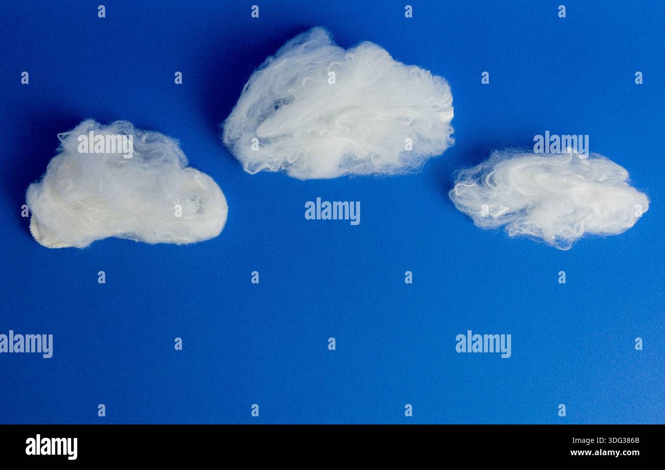 Composizione creativa e minimalista di nuvole bianche in fibra tessile su un solido sfondo blu, ideale per concetti di libertà. Foto Stock
