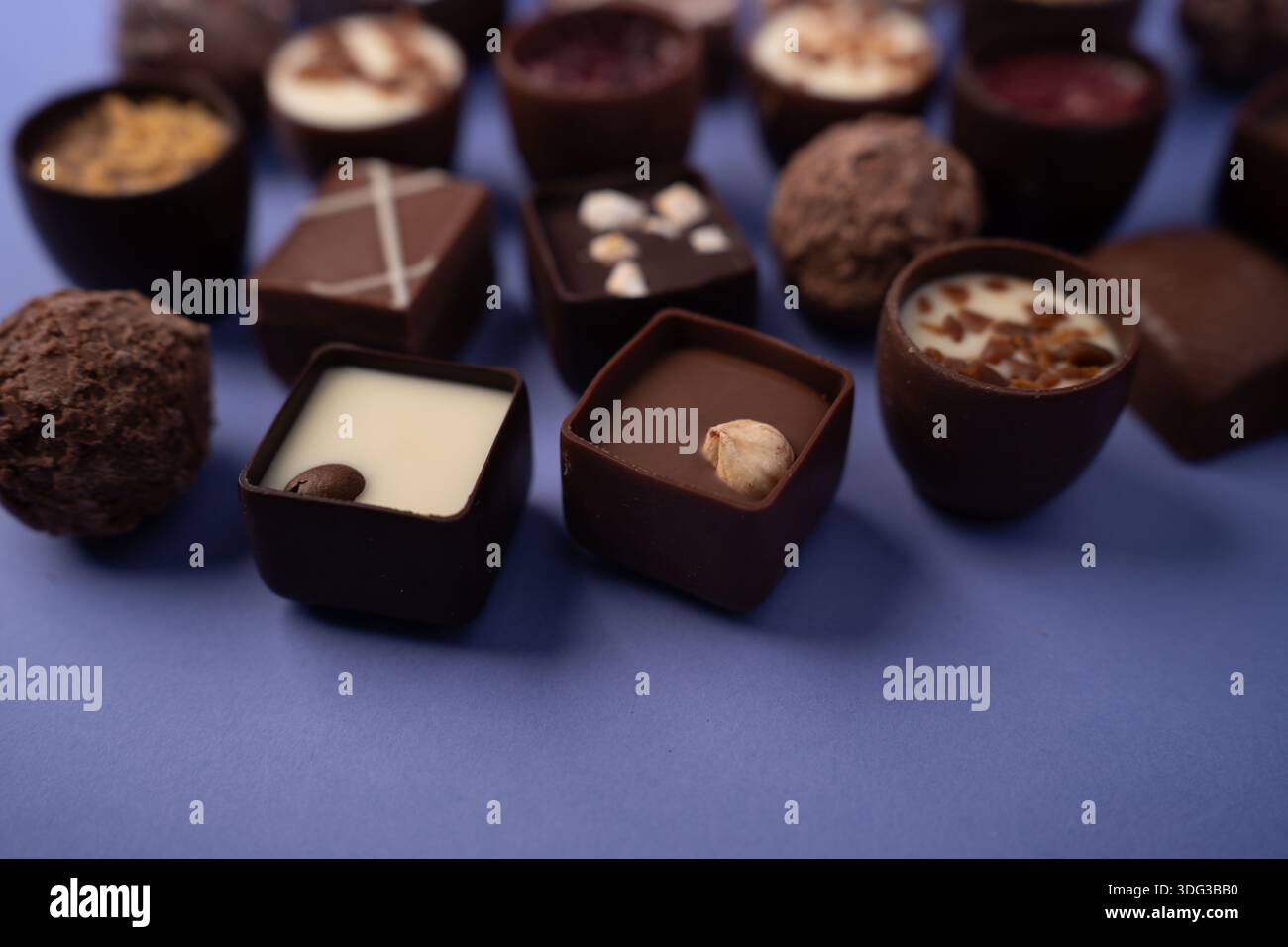 primo piano di bonbon artigianali al cioccolato e tartufi disposti su uno sfondo blu morbido, che mostra ganache lucide, accenti di nocciole e ripieno cremoso Foto Stock