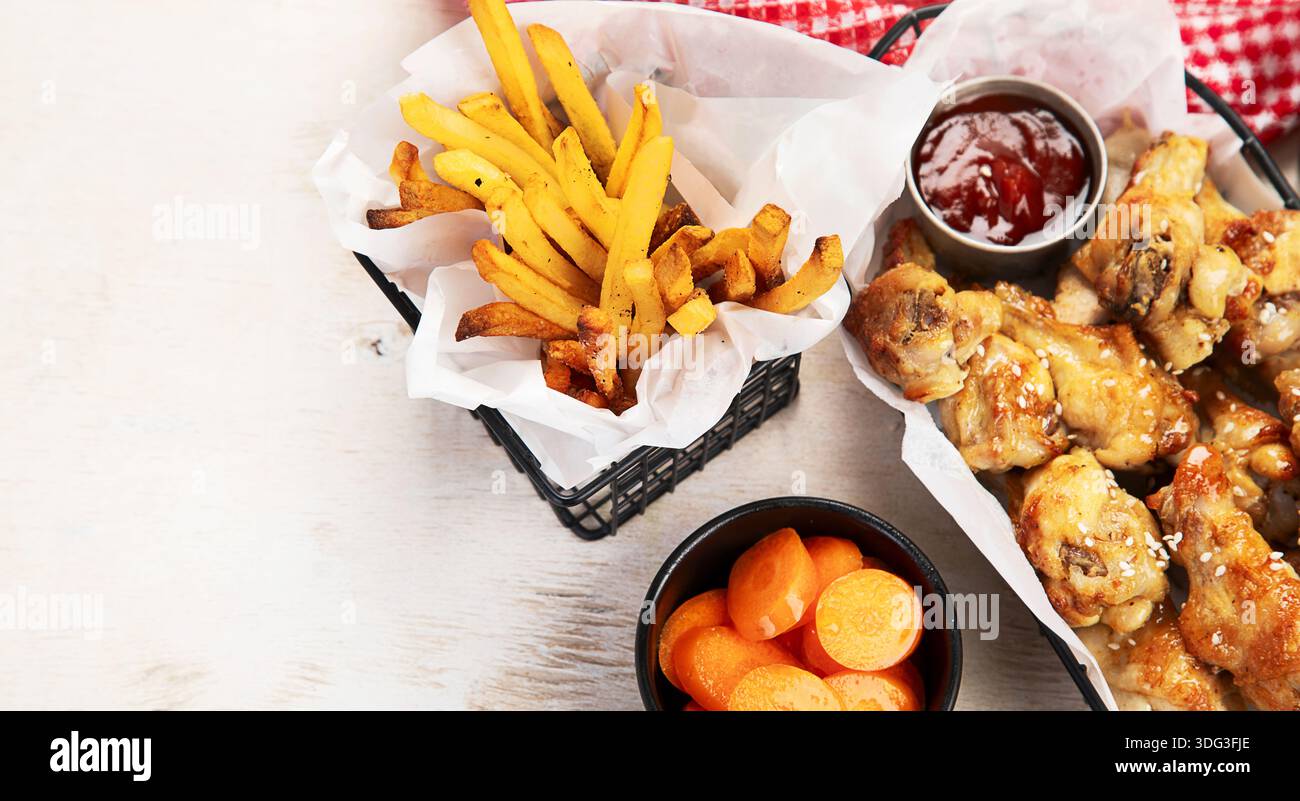 Ali di pollo fritte con salsa, patatine fritte e insalata su uno sfondo chiaro. Fast food. Vista dall'alto. Foto Stock