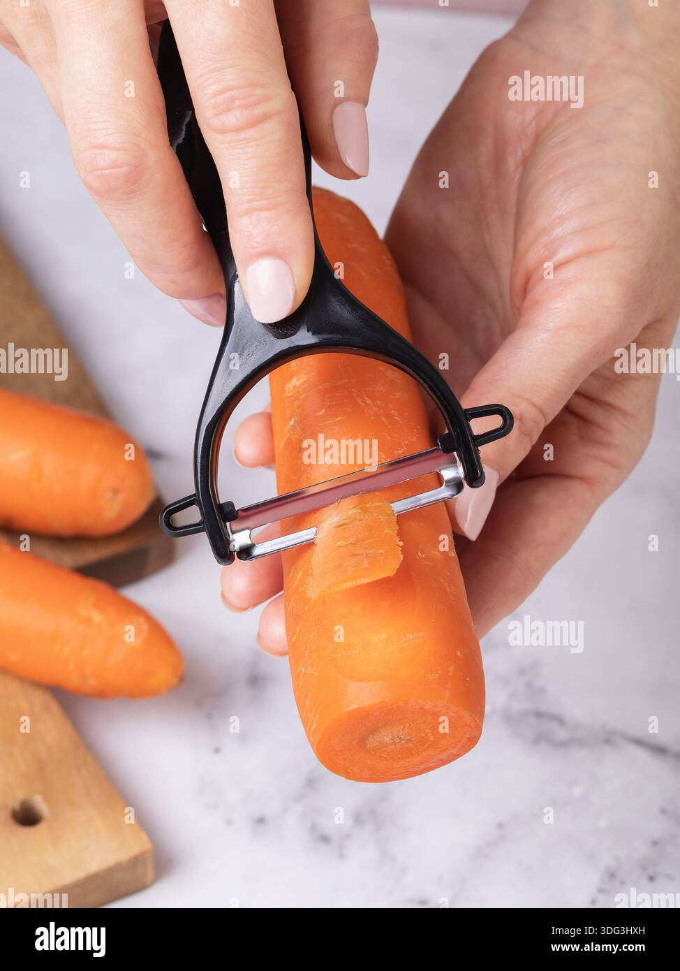 Una donna che sbuccia una carota con un pelapatate di verdure su un tavolo, primo piano, foto autentica, non generata dall'intelligenza artificiale. Foto Stock