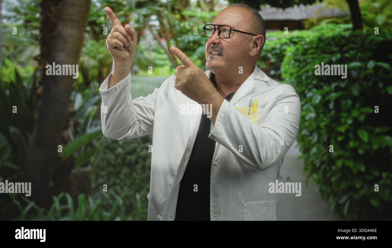 Uomo medico, ispanico anziano nel camice da laboratorio punta il dito verso l'alto con entrambe le mani vicino al passaggio del giardino, costruendo, indossando occhiali e penne tascabili; curiosit Foto Stock