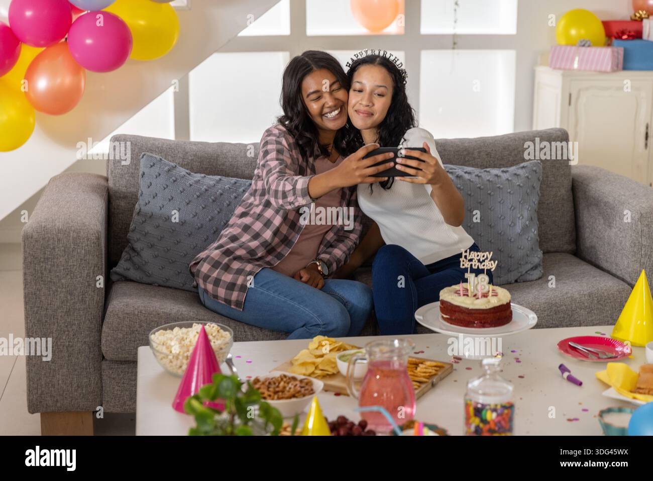 Mamma e figlia adolescente diverse che scattano selfie sul divano nel soggiorno del loft con il cellulare Foto Stock