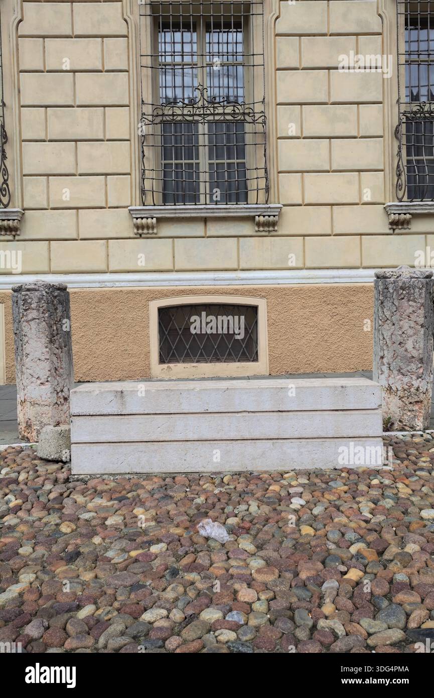 Panchina di pietra accanto al marciapiede tra due pilastri in una piazza acciottolata di una città italiana Foto Stock