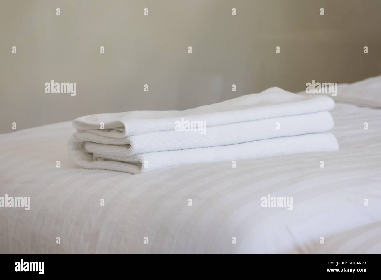 Una pila di asciugamani bianchi puliti piegati ordinatamente su un morbido letto in una comoda camera da letto che rappresenta il relax, l'ospitalità e la freschezza del bagno Foto Stock