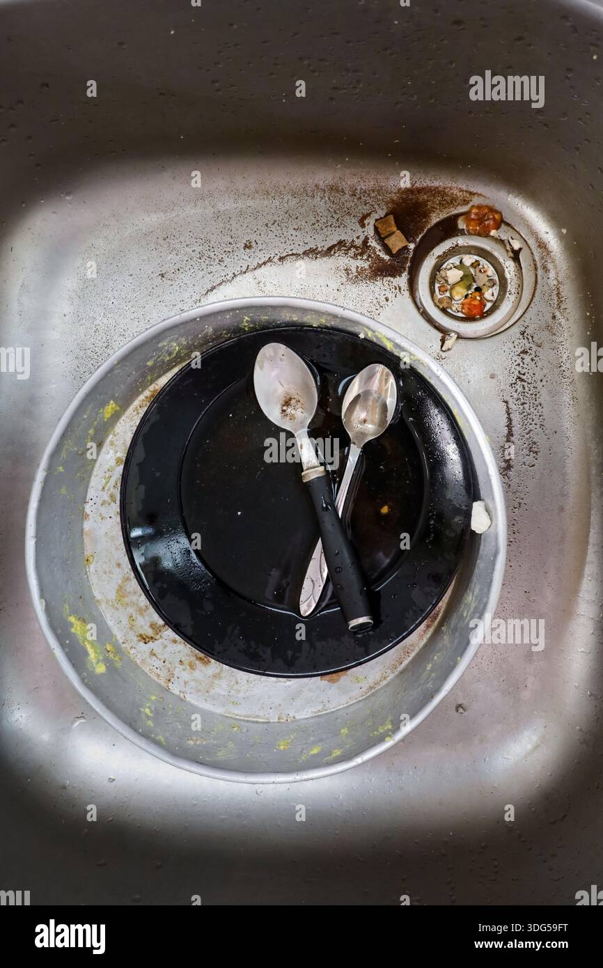 Una foto ravvicinata di un lavandino da cucina non sanitario pieno di piatti sporchi, cucchiai e alimenti residui, ideale per temi di vita domestica e igiene. Foto Stock