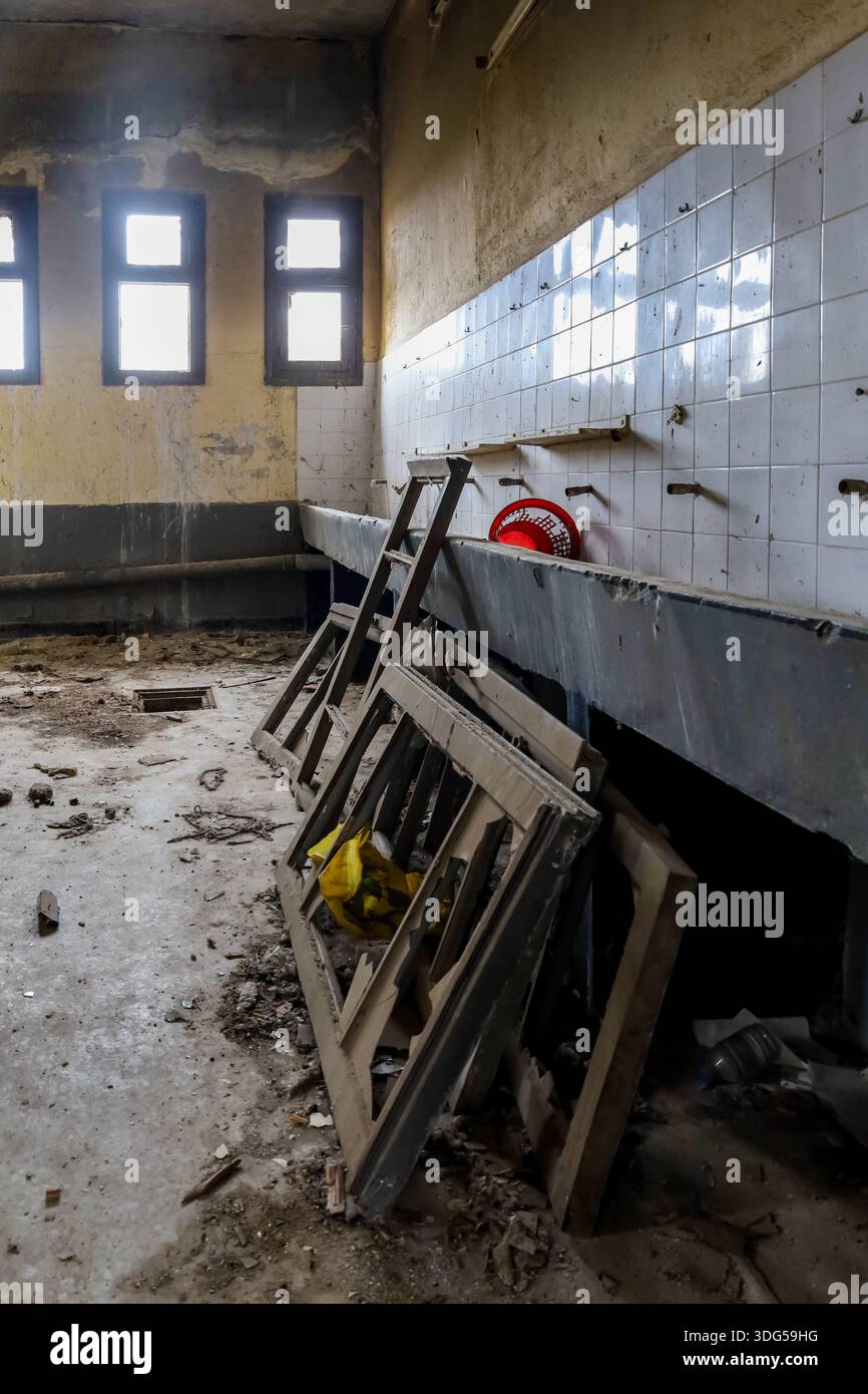 Interno di un bagno deteriorato in un edificio abbandonato, con lavabi rotti, telai delle finestre caduti e detriti sparsi. Foto Stock