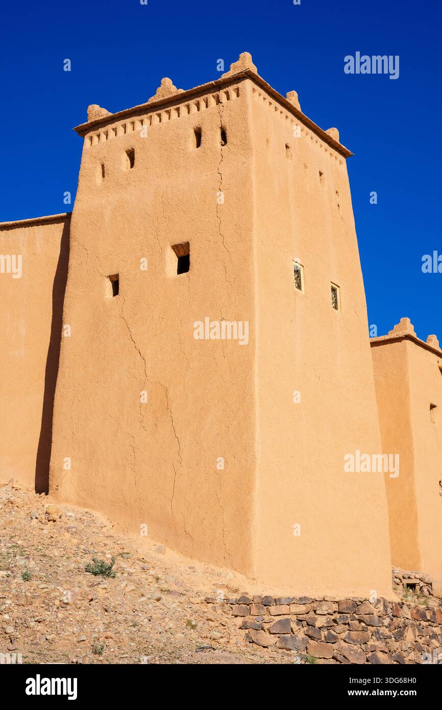 La torre della fortezza del deserto sotto il cielo blu con un'aspra base in pietra e muri in mattoni. Ouarzazate, Marocco Foto Stock