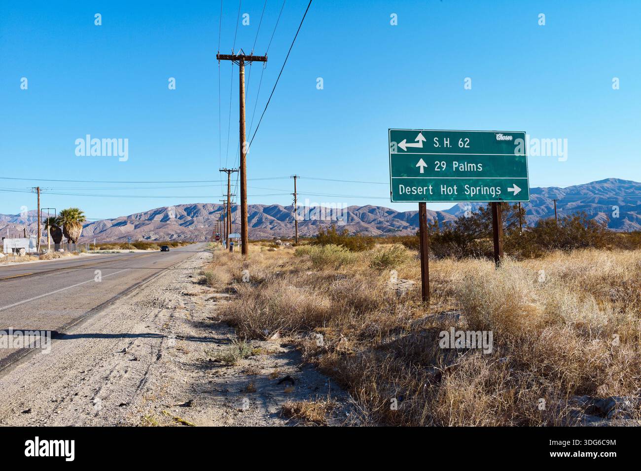 Lungo la strada nel deserto con un cartello che indica 29 Palms e Desert Hot Springs sotto il cielo limpido. STATI UNITI Foto Stock
