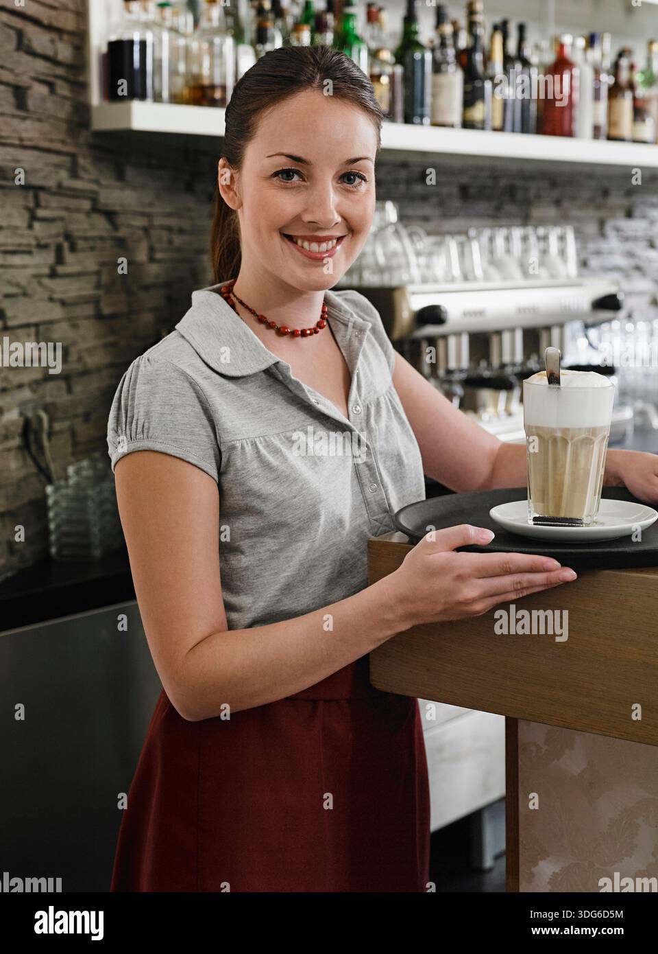 Donna sorridente in un bar che serve un latte con sfondo in pietra a strati. Germania Foto Stock