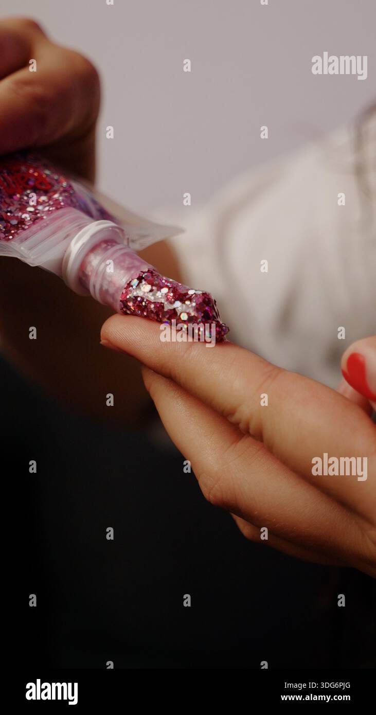 Un primo piano di mani che spruzzano o versano scintillante polvere cosmetica su un braccio. Foto Stock