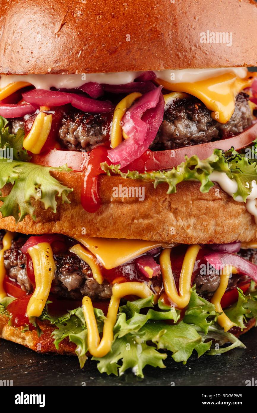Primo piano di un hamburger gourmet a due strati con succose polpettine di manzo, formaggio fuso, fette di cipolla fresche, lattuga croccante e salsa rossa ricca. Foto Stock