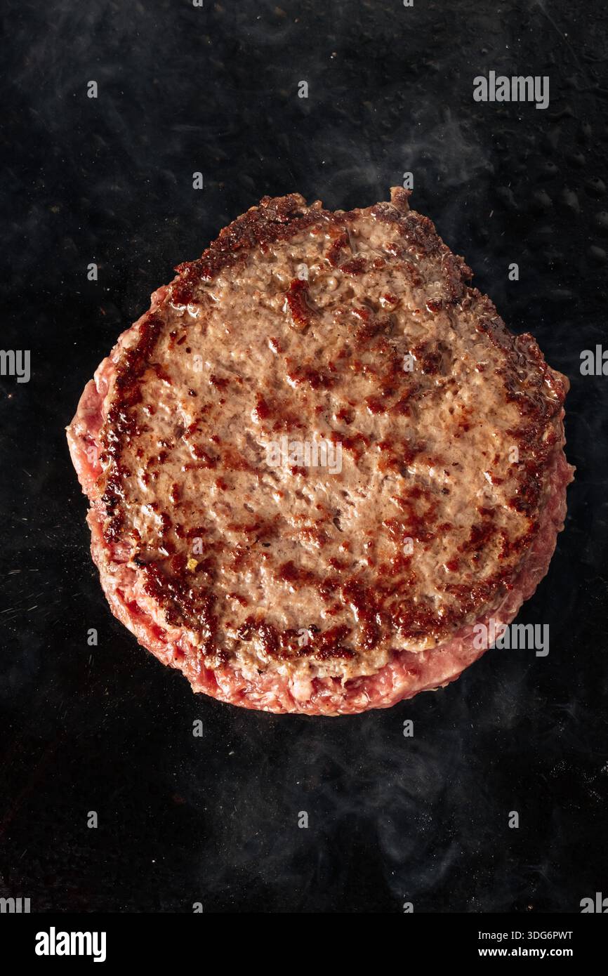 Primo piano di manzo grigliato su fiamme libere, con consistenza sfrigolante, segni di crosta e aumento del fumo. Cottura di carne succosa su una griglia barbecue calda. Foto Stock