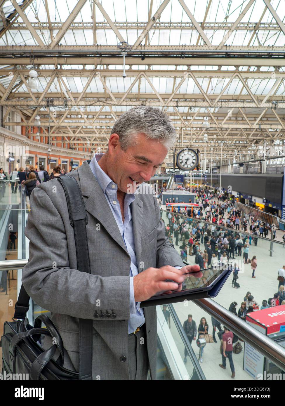 Uomini d'affari e TEAM DI computer tablet/comunicazioni ZOOM alla stazione ferroviaria di Waterloo di Londra tecnologia "On the Move" con pendolari e orologio dietro il Regno Unito Foto Stock
