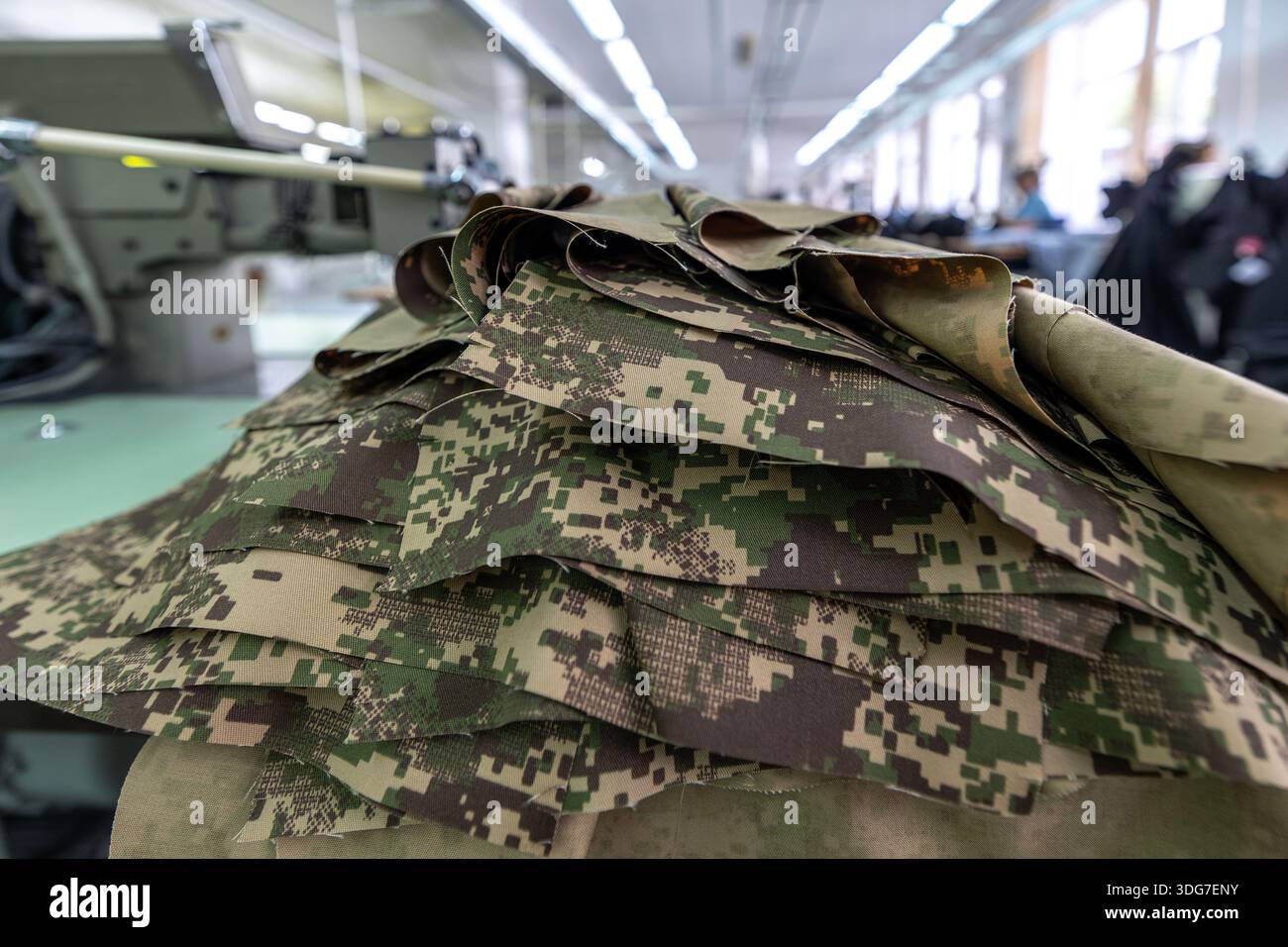Pila di capi in tessuto mimetico taglio per pantaloni militari. Primo piano di elementi tessili tattici pixelati preparati per cucire uniformi militari in professioni Foto Stock