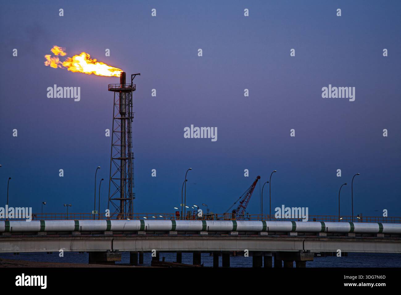Bruciando il gas in eccesso in un impianto di rigassificazione vicino a Huelva, in Spagna, al crepuscolo. Le strutture chimiche costiere sono sagomate contro il cielo serale. Foto Stock