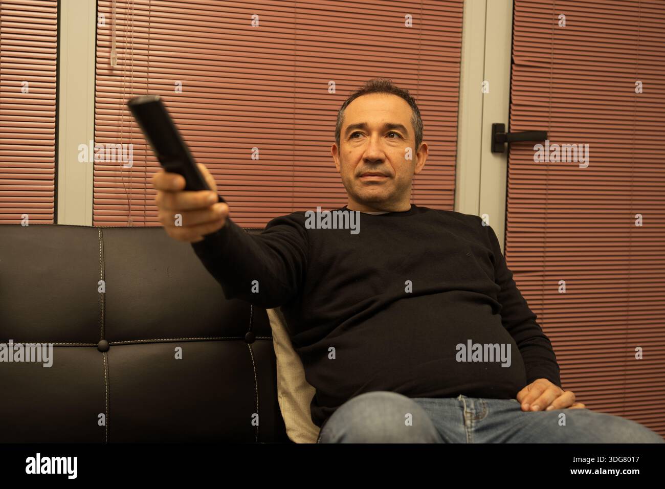 Uomo che si rilassa su un divano, tiene in mano un telecomando e si diverte a divertirsi Foto Stock