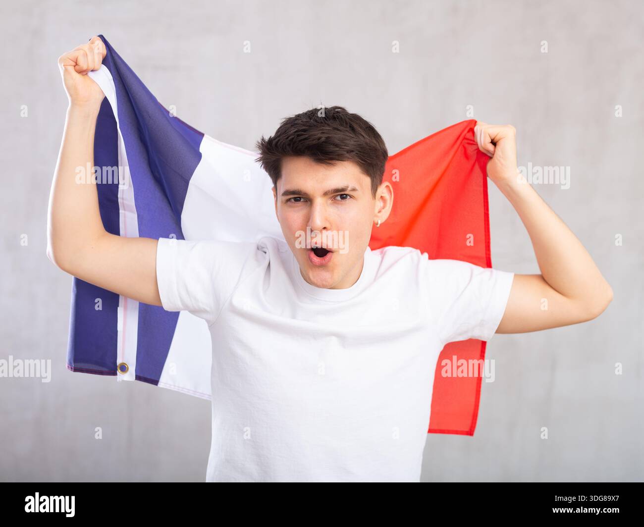Eccitato, attivo spettatore maschile detiene bandiera nazionale della Francia in mani e canti slogan popolare Foto Stock