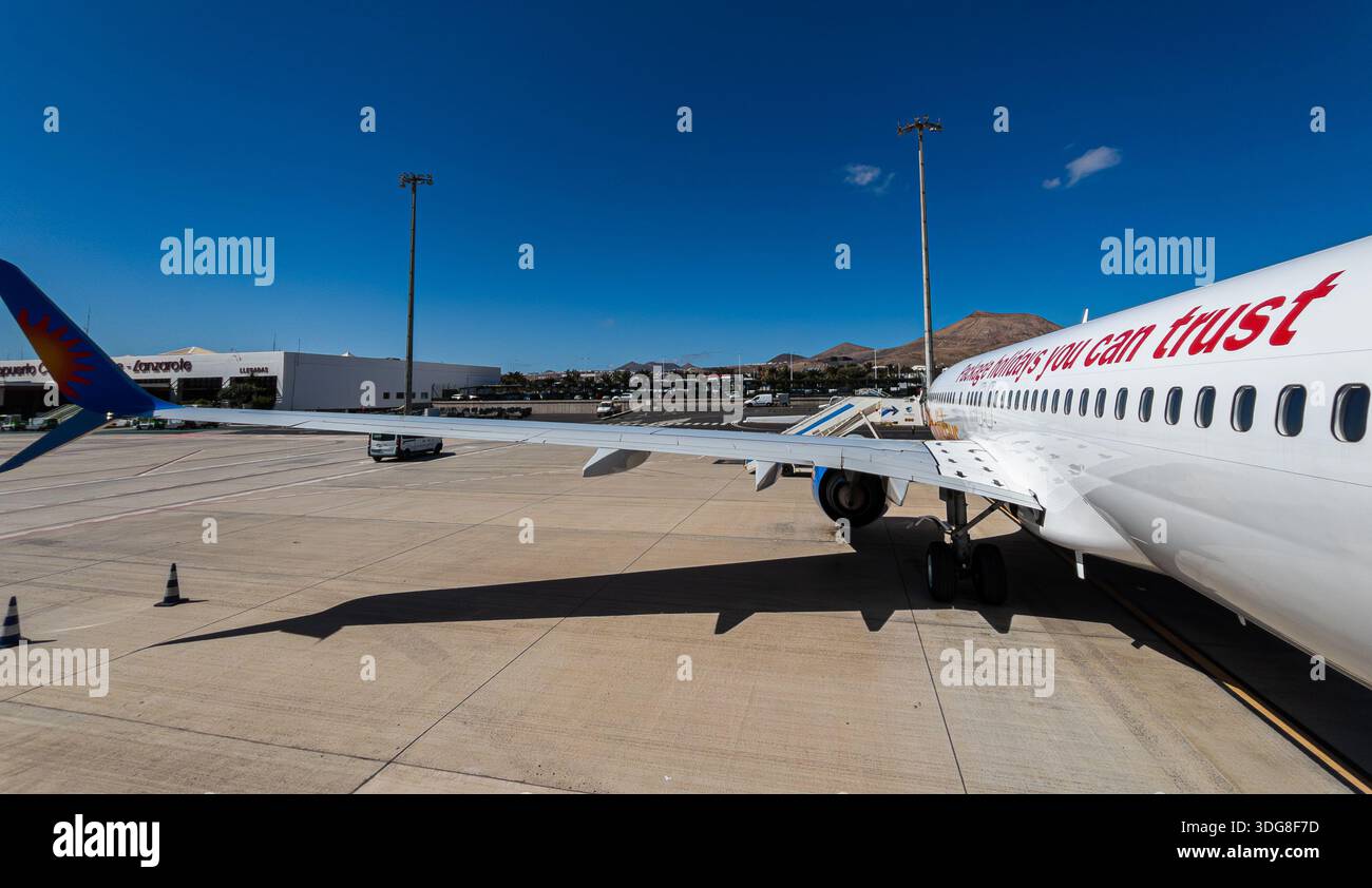 Aereo commerciale parcheggiato sull'asfalto dell'aeroporto con ala e motore visibili sotto il cielo azzurro Foto Stock