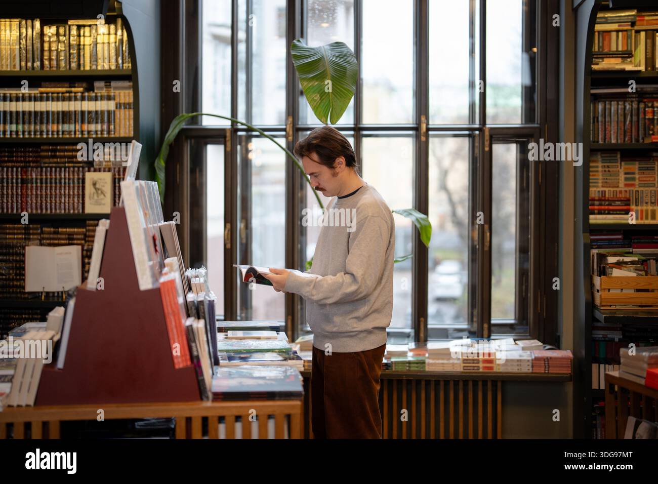 Uomo attento che sceglie i libri più venduti in libreria circondata da scaffali pieni di pubblicazioni. Foto Stock